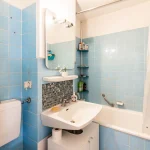 Badezimmer mit hellblauen Fliesen, weißem Waschbecken und Badewanne