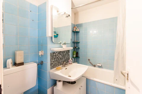 Badezimmer mit hellblauen Fliesen, weißem Waschbecken und Badewanne
