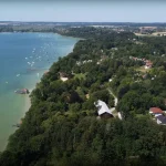 Luftaufnahme eines Baugrundstücks in Inning am See. Gezeigt sind ein See mit vielen Booten, umliegende Dächer der Ortsbebauung und Felder. Markierter Punkt könnte Ziel für Immobilienerwerb sein.