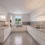 Moderne Küche in Weiß mit schwarzen Arbeitsflächen, integrierten Geräten und Kochinsel. An der Wand Regale mit Büchern, dekorative Elemente. Großes Fenster mit Blick ins Freie und Esstisch mit bunten Platzsets.