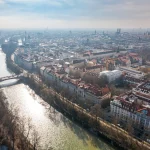 Blick auf die Isar mit grünen Ufern und Stadtkulisse im Hintergrund bei klarem Himmel.