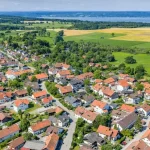 Luftaufnahme von Frieding, zeigt eine dicht bebaute Wohnsiedlung mit vielen Einfamilienhäusern und umgebenden Grünflächen und Feldern. Die Anordnung der Häuser ist organisiert, umgeben von Straßen und Bäumen.