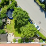 Vogelperspektive auf einen privaten Garten mit Rasenfläche, Trampolin, Terrasse und angrenzender Straße.