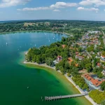 Luftaufnahme von Herrsching am Ammersee zeigt dicht bebaute Wohngegenden, grüne Flächen und den klaren Ammersee mit Booten. Ideal für Immobilienmakler, die in attraktiven Lagen vermitteln wollen.