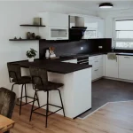 Moderne, offene L-Küche in Weiß und Schwarz mit Bar-Theke, Barhockern und kombiniertem Fliesen- und Parkettboden.