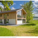 Neubau Idee: Modernes Holzhaus mit großen Glasfronten und Blick auf einen See im Grünen