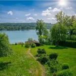 Seegrundstück am Pilsensee mit großem Garten, altem Baumbestand und kleinem Bootshaus unter strahlend blauem Himmel