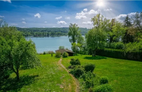 Seegrundstück am Pilsensee mit großem Garten, altem Baumbestand und kleinem Bootshaus unter strahlend blauem Himmel