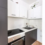 Moderne Einbauküche mit weißen Oberschränken, dunklen Unterschränken, Cerankochfeld und Edelstahlspüle in einer Wohnung