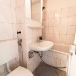Kompaktes Duschbad einer Wohnung mit hellen Wandfliesen, Waschbecken, Toilette und Badewanne