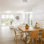 Moderner, offener Wohn-Essbereich mit hellem Holztisch, cremefarbenen Stühlen, weißem Sofa und Zugang zum Garten.