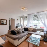 Heller und gemütlicher Wohnbereich mit großer Couch, Glastisch und Balkonzugang