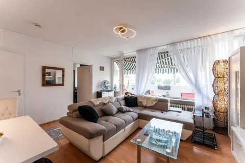 Heller und gemütlicher Wohnbereich mit großer Couch, Glastisch und Balkonzugang